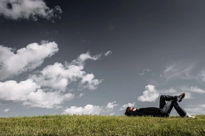 Un homme allongé dans l'herbe regarde les nuages pensif